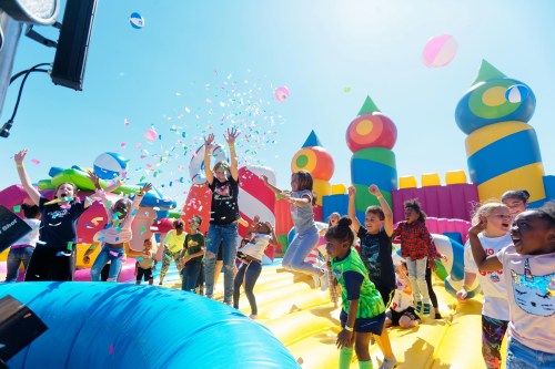 A lively scene of children jumping on a colorful inflatable bounce house, surrounded by beach balls and confetti.