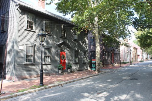 Historic houses with dark wooden exteriors and red doors, lined along a tree-shaded street.