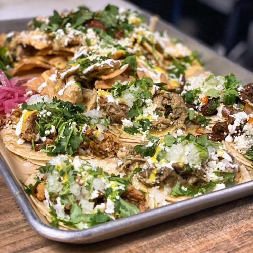 A tray of colorful tacos topped with cilantro, onions, cheese, and various meats, garnished with pickled onions.