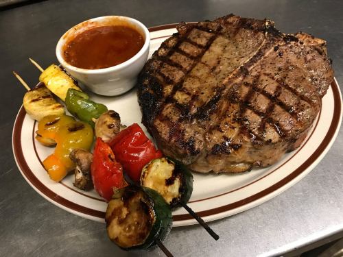 A grilled steak with a side of barbecue sauce and skewered vegetables on a plate.