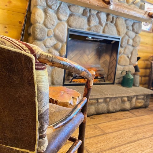 A cozy wooden chair in front of a stone fireplace, creating a warm and inviting atmosphere.