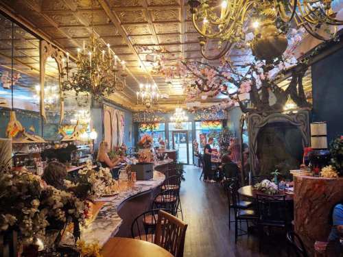 Elegant restaurant interior with chandeliers, floral decor, and a cozy atmosphere, featuring tables and a bar area.