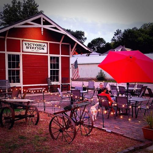 A cozy outdoor seating area with string lights, a red umbrella, and a historic building labeled "Victoria Station."
