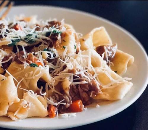 A plate of pasta with meat sauce, topped with grated cheese and herbs, served on a dark table.