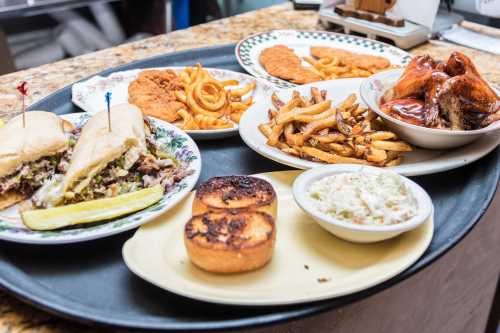 A tray of various dishes including sandwiches, fried chicken, curly fries, coleslaw, and cornbread.