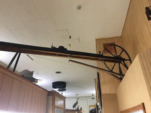 A large, vintage pulley system mounted on a wooden wall in a museum setting.