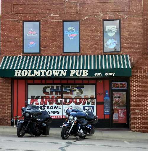 Exterior of Holmtown Pub with two motorcycles parked outside and various beer advertisements on the windows.