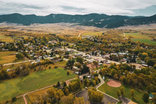 Aerial view of a small town surrounded by green fields and mountains, with autumn foliage in the trees.