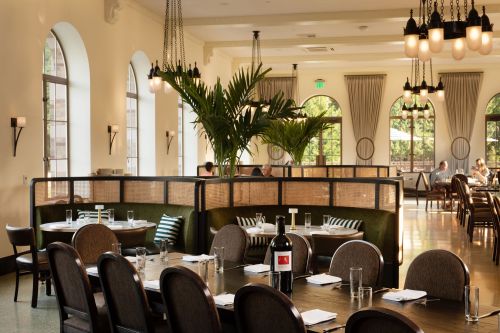 A stylish restaurant interior featuring green booths, a large dining table, and elegant lighting.