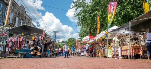 A bustling outdoor market with vendors, colorful tents, and visitors browsing under a bright blue sky.