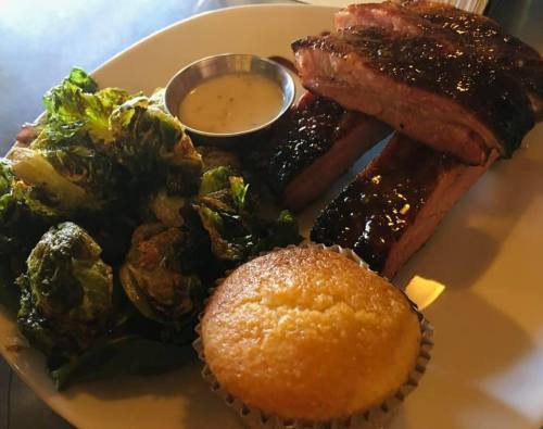 A plate featuring glazed ribs, a side of sautéed greens, and a cornbread muffin.