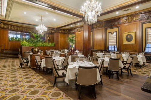 Elegant restaurant interior with wooden decor, chandeliers, and neatly arranged tables set for dining.