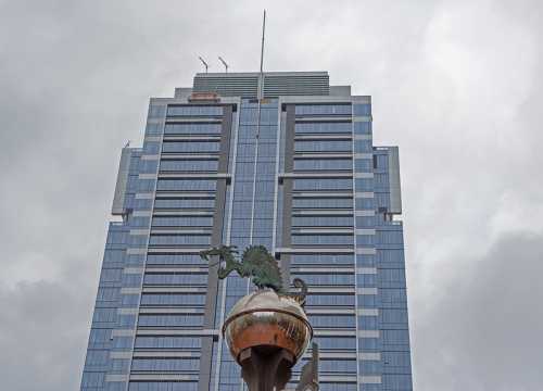 A tall modern skyscraper under a cloudy sky, featuring a decorative dragon statue in the foreground.