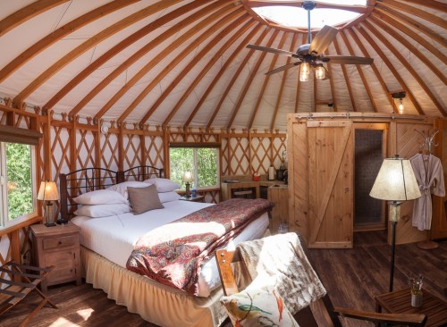 Cozy yurt interior featuring a queen bed, wooden accents, and natural light from a skylight.
