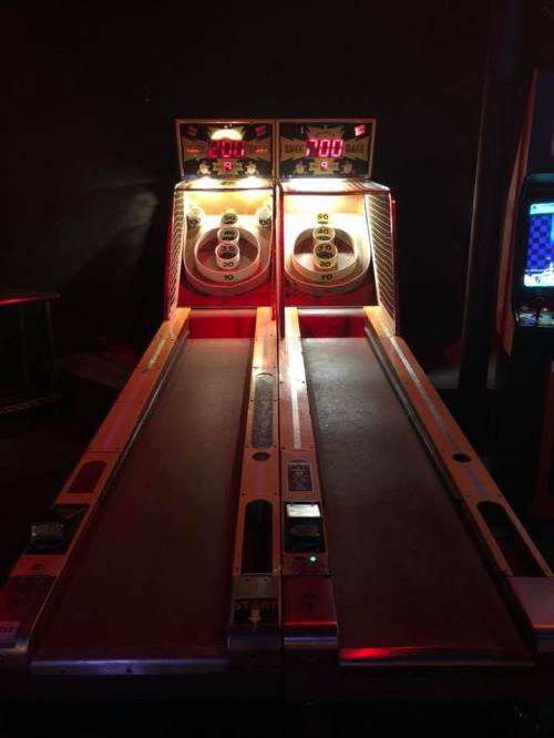 Two illuminated skee-ball machines side by side, displaying scores of 200 and 700, in a dimly lit arcade.