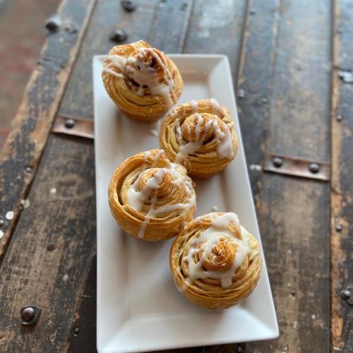 Four glazed pastry rolls arranged on a white plate, resting on a rustic wooden table.