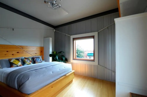 Cozy bedroom featuring a wooden bed, gray bedding, and a large window with natural light.