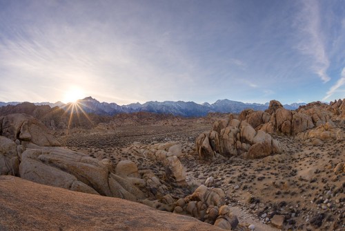 A panoramic view of rocky terrain at sunset, with mountains in the background and a clear sky.