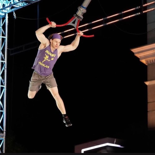 A contestant swings on a trapeze during an obstacle course challenge, showcasing athleticism and determination.