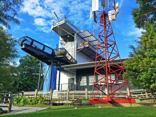 A unique modern building with a slide, windmill, and colorful exterior against a blue sky.