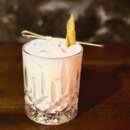 A frothy cocktail in a crystal glass, garnished with a twist of citrus peel on a wooden surface.