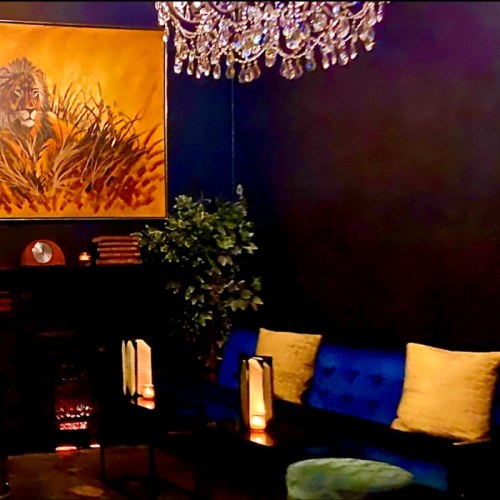A cozy room featuring a lion painting, a chandelier, plants, and stylish seating with warm lighting.