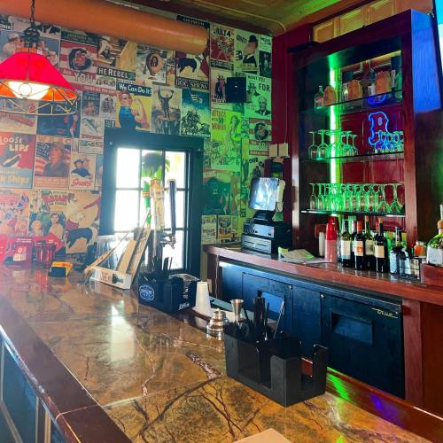 A vibrant bar with a colorful wall of vintage posters, a polished countertop, and shelves of drinks in the background.