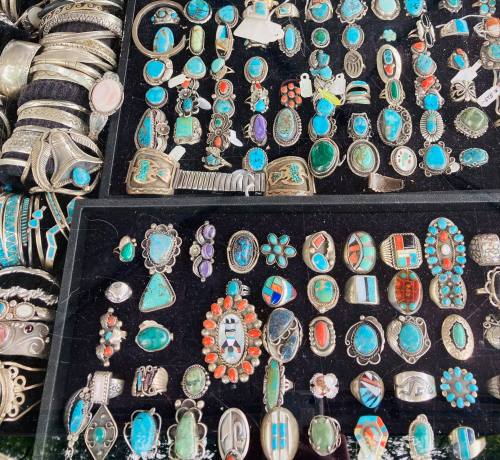 A display of various turquoise and silver jewelry pieces, including rings and pendants, arranged on a black background.