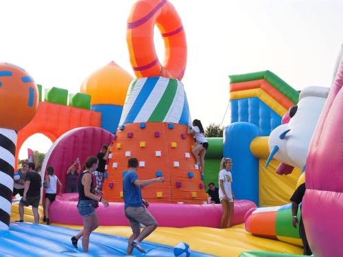 A colorful inflatable playground with people climbing and playing on various structures under a sunny sky.