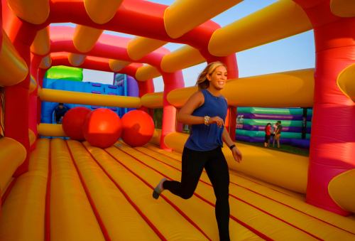 A person runs joyfully inside a colorful inflatable bounce house with large red balls.