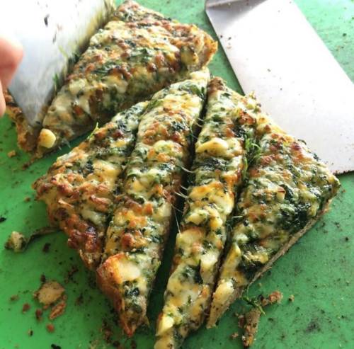 A freshly cut slice of cheesy spinach bread on a green cutting board.
