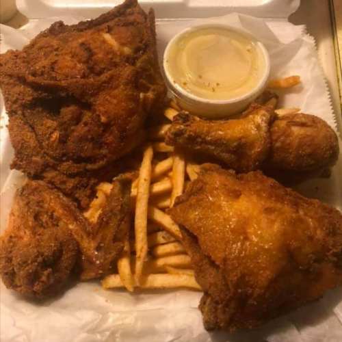 A takeout box with crispy fried chicken pieces and a side of French fries, accompanied by a small container of sauce.