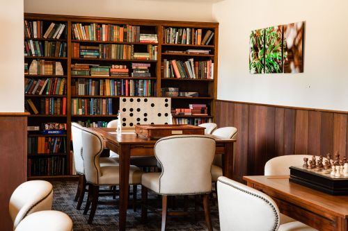 Cozy library with wooden bookshelves, a chess set, and a game table surrounded by upholstered chairs.