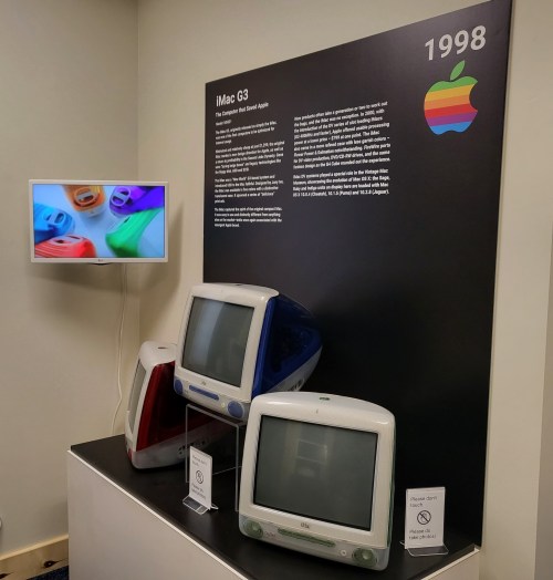 Display of the 1998 iMac G3 in various colors, alongside a screen showcasing colorful iMac designs.