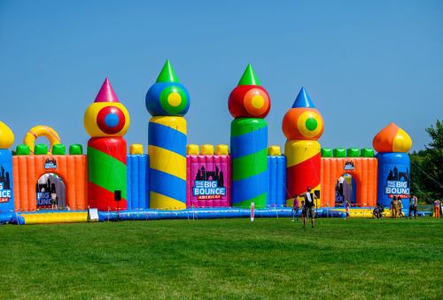 Colorful inflatable bounce house with tall towers and bright patterns, set on a grassy field under a clear blue sky.