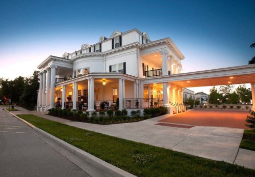 A grand white mansion with columns, illuminated at dusk, featuring a wide driveway and landscaped surroundings.