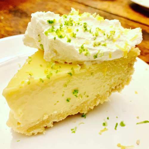 A slice of lemon pie topped with whipped cream and lime zest on a white plate.