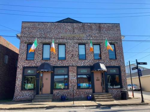A brick building with Irish flags hanging, featuring two entrances and a clear blue sky above.