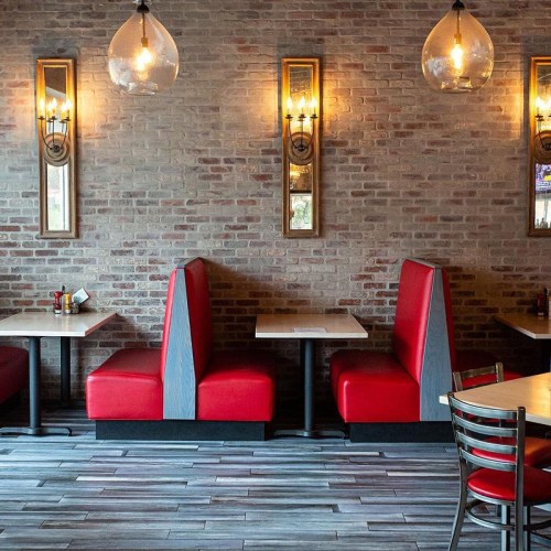 Cozy restaurant interior with red booths, wooden tables, and warm lighting against a brick wall.