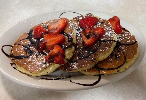 A plate of pancakes topped with sliced strawberries, chocolate drizzle, and powdered sugar.