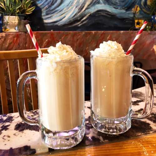 Two frosty mugs filled with creamy beverages topped with whipped cream and red-and-white striped straws.
