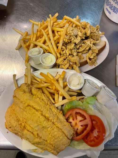 Two plates of food: one with fried fish, lettuce, tomato, and fries; the other with fried chicken and fries.