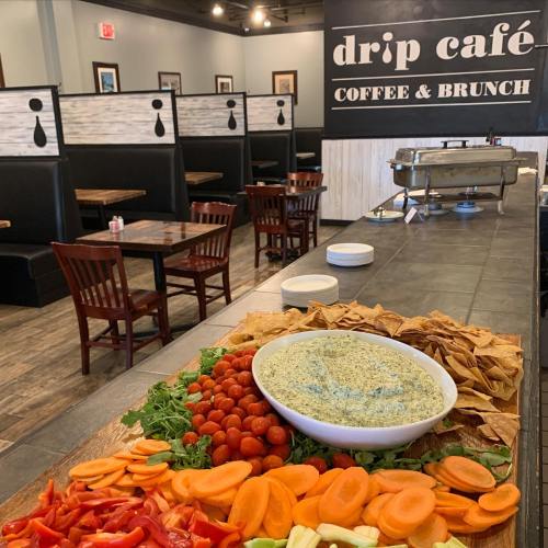A vibrant spread of fresh vegetables, chips, and dip on a table in a cozy café setting.