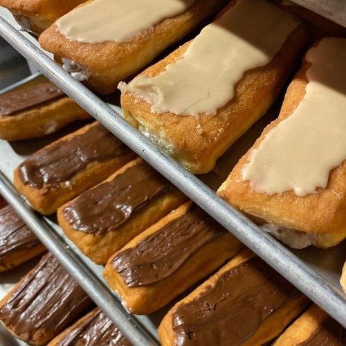 A tray of pastries with creamy toppings: some are coated in chocolate, others in a light beige frosting.