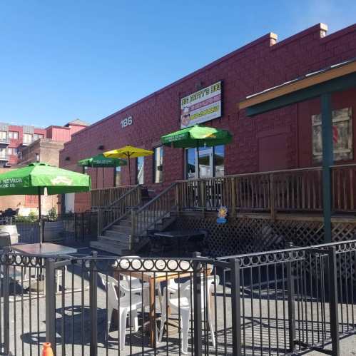 Outdoor seating area of a restaurant with green umbrellas, wooden steps, and a red brick building in the background.