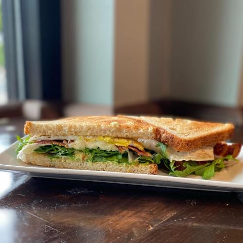 A close-up of a sandwich with layers of lettuce, ham, and egg, served on toasted bread on a white plate.