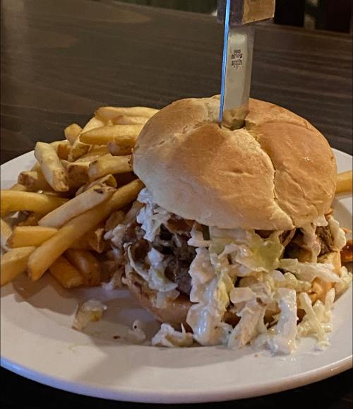 A hearty burger topped with coleslaw, served with a side of crispy fries and a knife inserted into the bun.