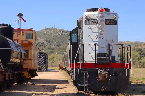 A vintage train engine parked beside a red caboose, with hills in the background under a clear blue sky.