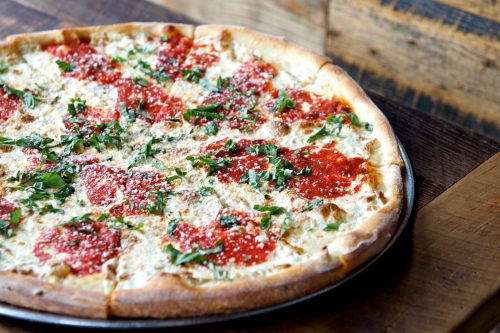 A freshly baked pizza topped with marinara sauce, cheese, and fresh herbs on a wooden table.