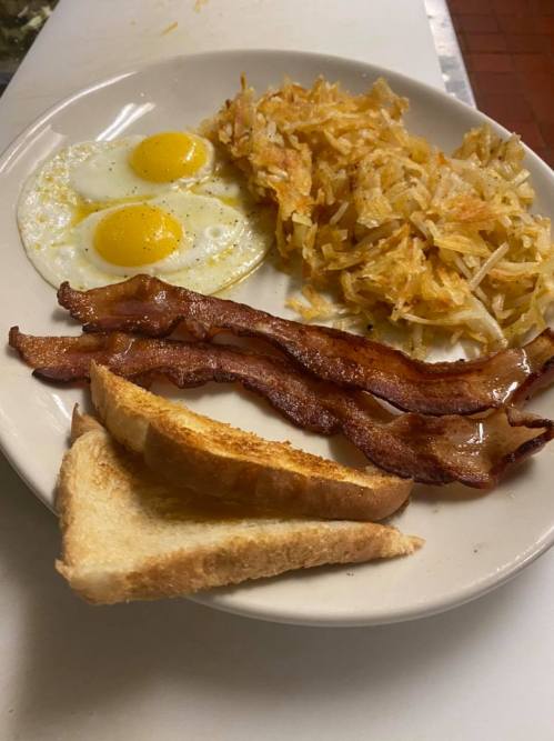A plate of breakfast featuring two sunny-side-up eggs, hash browns, crispy bacon, and toasted bread.